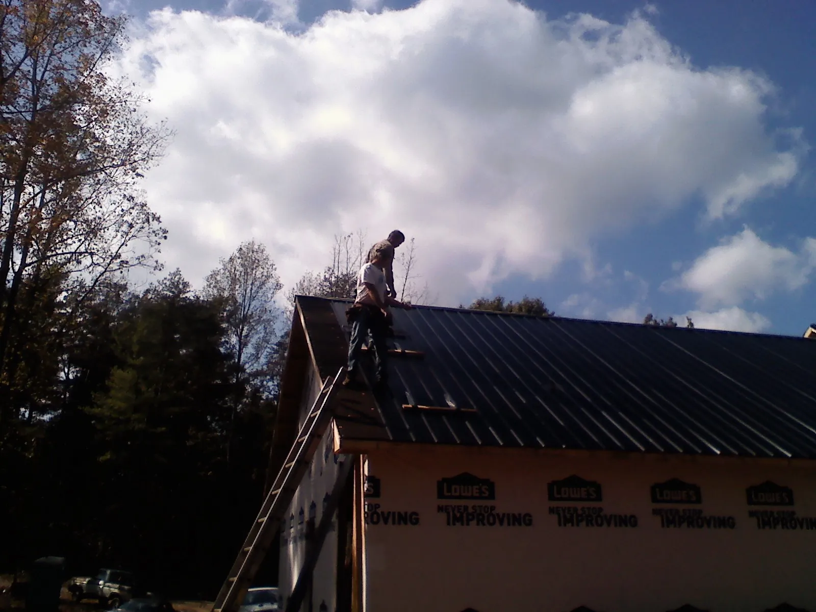 Roofer fastening dark metal panels high against a cloudy sky, from a Roof Inspection job in Addy