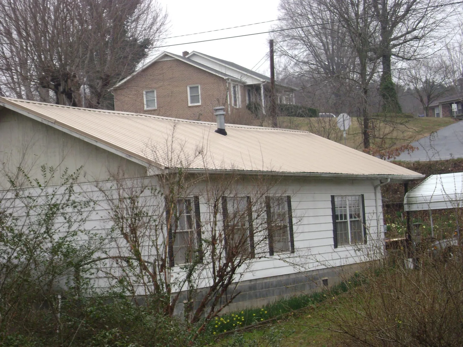 Tan metal roof on a white sided house set into a hillside — Commercial Roofing by Roofing Brothers in Addy